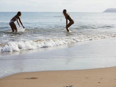 Dwie osoby bawią się w wodzie przy piaszczystej plaży nad morzem.