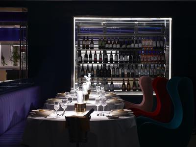 Elegancko nakryty stół z kieliszkami i butelkami, kolorowe krzesła w ciemnej restauracji.