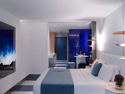 Chambre d'hôtel moderne avec grand lit, couverture bleue et TV murale.