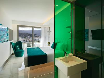 Nowoczesny pokój hotelowy z dużym oknem, podwójnym łóżkiem i łazienką z zieloną przegrodą.