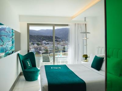 Chambre d'hôtel moderne avec lit double, accents verts et vue sur la montagne par de grandes fenêtres.