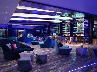 Nowoczesny bar hotelowy z niebieskim oświetleniem i wygodnymi miejscami do siedzenia.