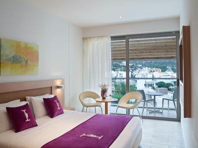 Chambre d'hôtel lumineuse avec lit double, accents violets et terrasse donnant sur le port.