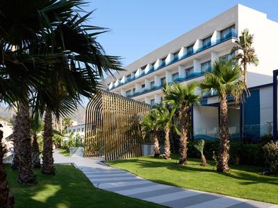 Complexe hôtelier moderne avec des palmiers et un chemin sous un ciel bleu.
