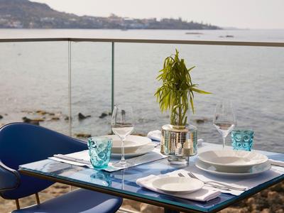 Table dressée sur une terrasse avec vue sur la mer et chaises bleues.