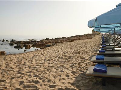 Plage de sable avec chaises longues sous parasols bleus au bord d'une mer calme.