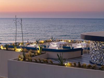 Terrasse moderne avec espace lounge et vue sur la mer au coucher du soleil.