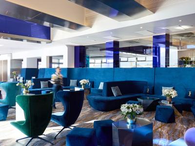 Salon d'hôtel moderne avec sièges bleus et grandes fenêtres.