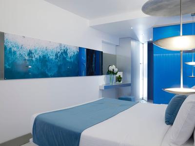 Chambre d'hôtel moderne aux tons bleus et blancs avec une peinture représentant la mer.