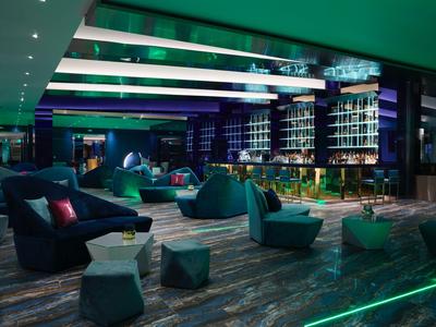 Salon d'hôtel moderne avec sièges élégants, éclairage d'ambiance et bar.