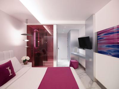 Chambre d'hôtel moderne avec lit blanc, accents roses et télévision murale.