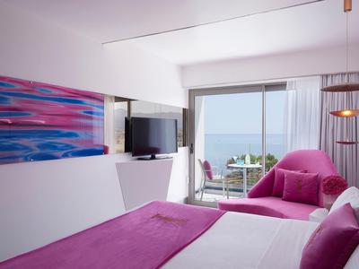 Chambre d'hôtel moderne avec accents violets, vue sur la mer et balcon.