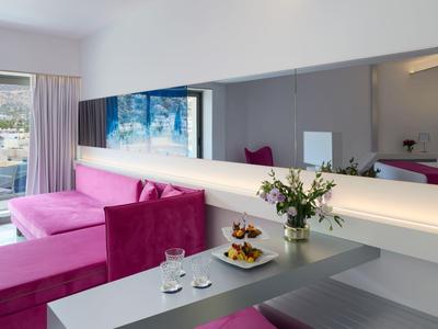 Chambre d'hôtel moderne avec canapé rose, grand miroir et vue sur balcon.