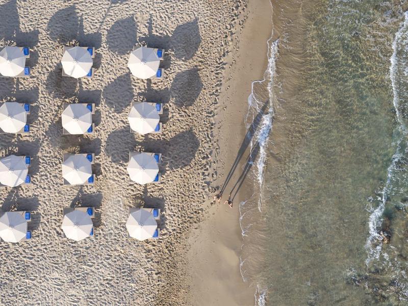 Plaża z białymi parasolami ułożonymi w rzędach przy przejrzystej wodzie.