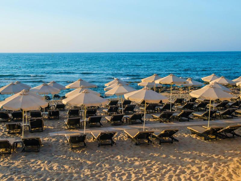 Plaża z rzędami leżaków i parasoli nad morzem o zachodzie słońca.