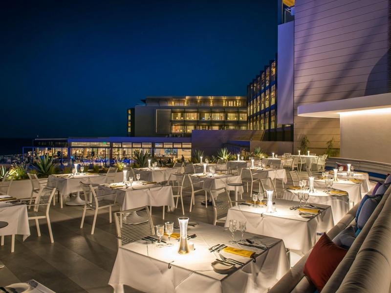 Elegancki taras restauracyjny hotelu oświetlony nocą z nakrytymi stołami i białymi krzesłami.