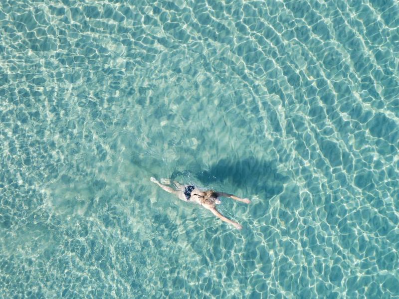 Osoba pływa w przezroczystej, turkusowej wodzie widziana z góry.