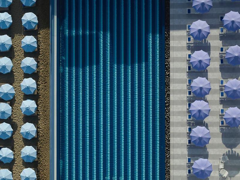 Długi niebieski basen z parasolami ułożonymi po obu stronach, widok z lotu ptaka hotelu.