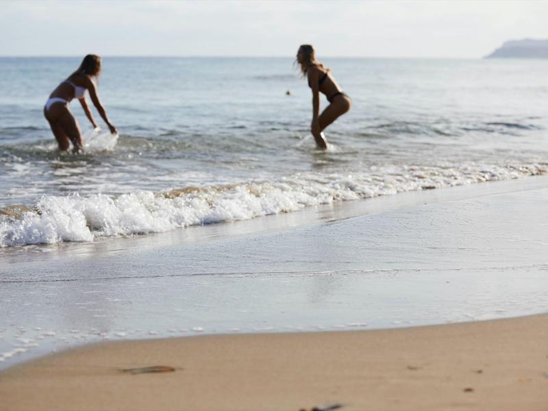 Dwie osoby bawią się w wodzie przy piaszczystej plaży nad morzem.