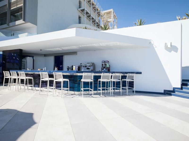 Nowoczesny bar na zewnątrz z białymi wysokimi krzesłami pod daszkiem przy białym budynku.