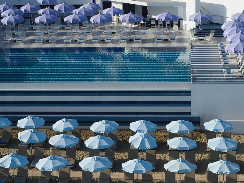 Nowoczesny basen hotelowy z leżakami i niebieskimi parasolami, symetryczny widok z góry.