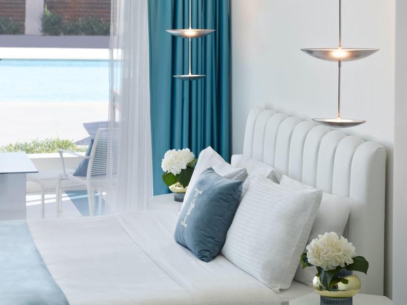 Nowoczesny salon z białą sofą, niebieskimi poduszkami i wiszącymi lampami, widok na basen przez okno.