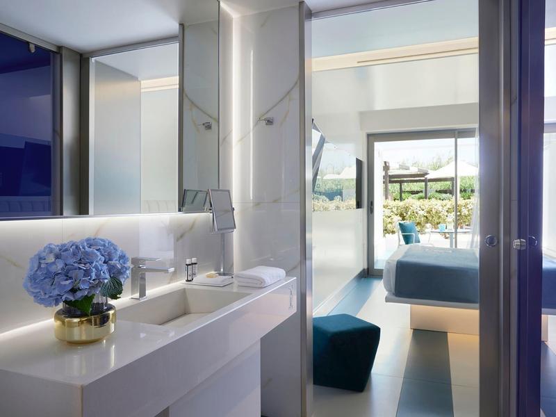 Nowoczesny wnętrze pokoju hotelowego z niebieskimi dekoracjami i wyjściem na słoneczny taras.