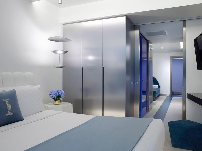 Nowoczesny pokój hotelowy z podwójnym łóżkiem, niebieskimi dekoracjami i minimalistycznymi meblami.