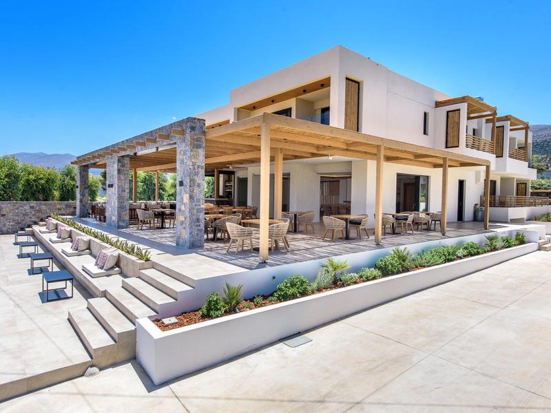 Modern vakantiehuis met groot terras en zitplaatsen onder een heldere blauwe lucht.