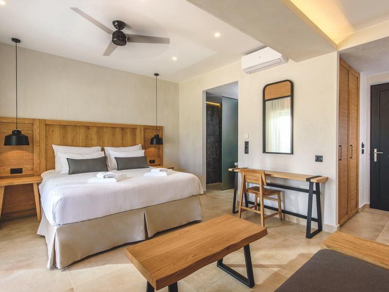 Modern hotelkamer met tweepersoonsbed, plafondventilator en eenvoudig houten meubilair.