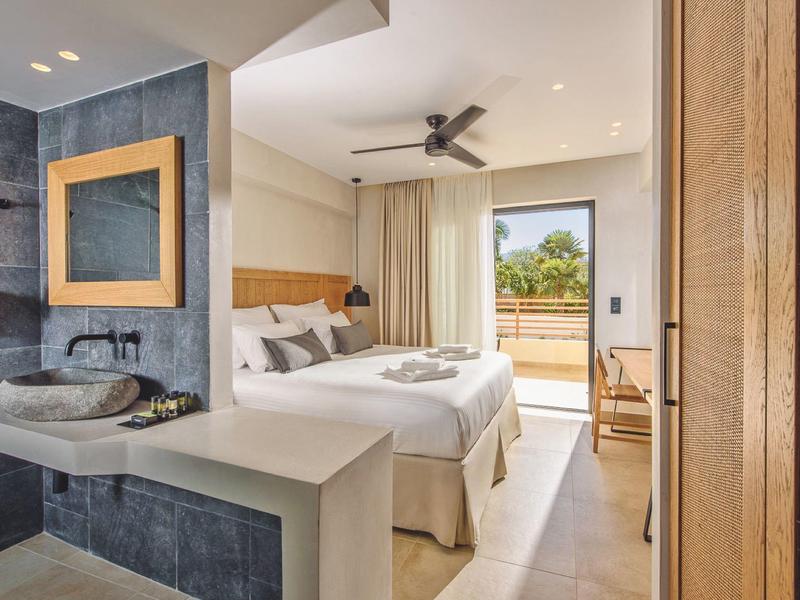 Moderne hotelkamer met twee bedden, open badkamer en balkon met uitzicht op groen.