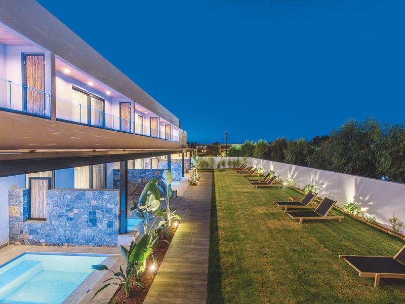 Moderne hotel tuin met ligstoelen, gras en verlichte glazen balustrades bij schemering.