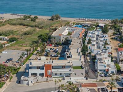 Complex hôtelier moderne avec piscine et espaces verts au bord de la mer, entouré de routes et parkings.