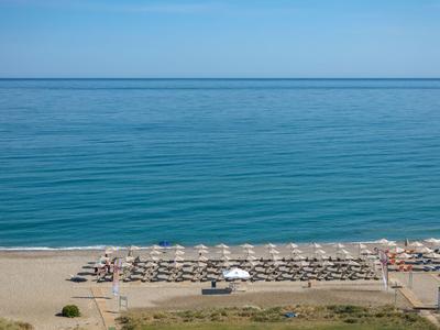 Plage avec parasols et chaises longues devant une mer bleue calme sous un ciel clair.