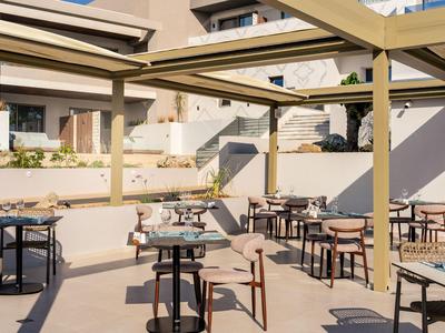 Terrasse extérieure d'hôtel avec tables, chaises et structure de pergola au soleil.