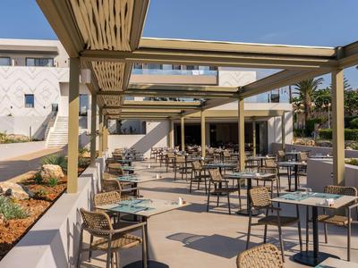 Terrasse extérieure avec tables et chaises devant un bâtiment d'hôtel clair sous un ciel bleu.
