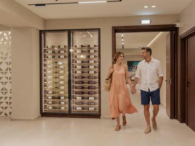 Un couple marche dans le couloir de l'hôtel devant des casiers à vin au mur.