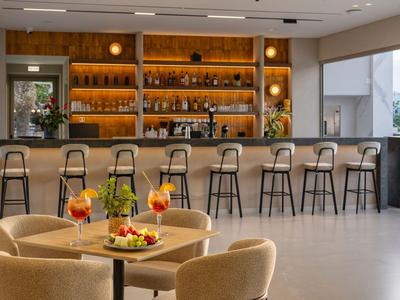 Bar d'hôtel moderne avec comptoir haut, tabourets de bar et coin salon confortable avec boissons.