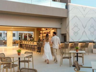 Un couple se dirige vers un bar d'hôtel moderne avec des chaises et des tables à l'extérieur.