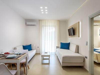 Chambre d'hôtel lumineuse avec deux canapés, coin repas et accès au balcon.
