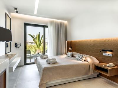 Chambre d'hôtel moderne avec lit double, TV, table de nuit et porte-balcon avec vue sur des palmiers.