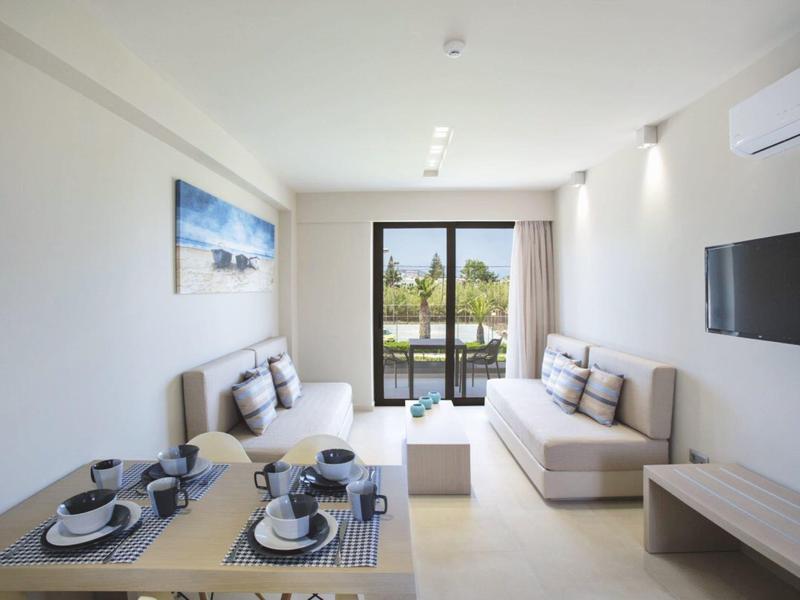 Sala luminosa con dos sofás, mesa de comedor y balcón con vista verde.