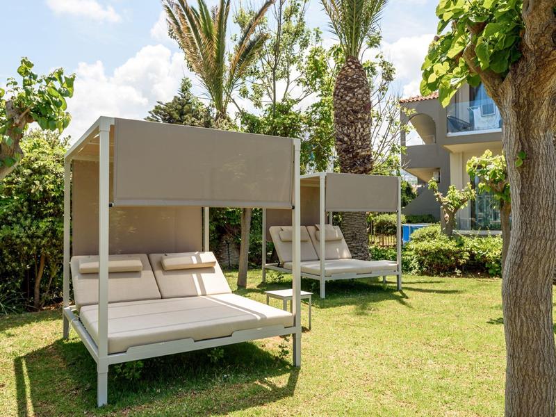 Dos cómodas camas modernas con toldos en el jardín de un hotel bajo el sol.