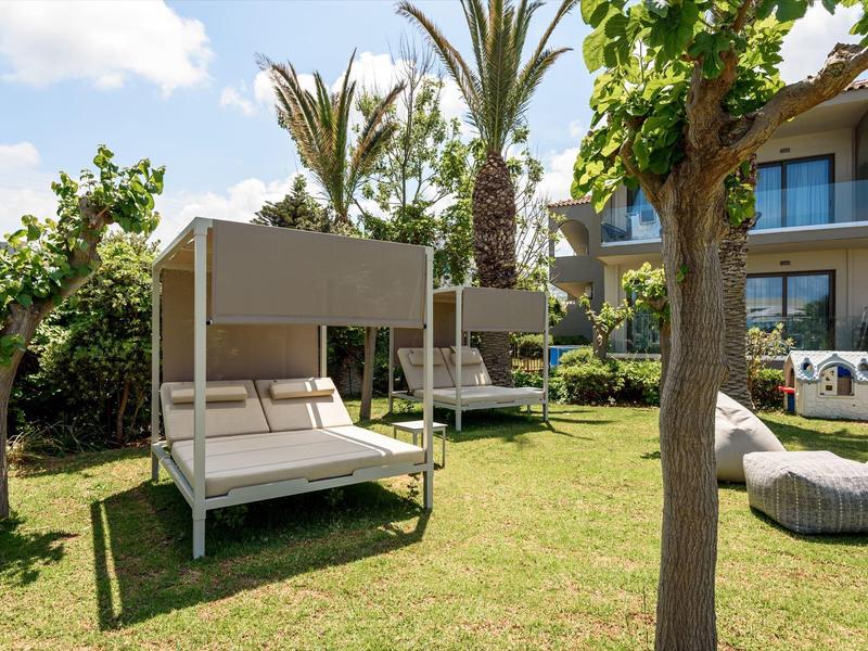 Área de jardín de hotel verde con tumbonas, palmeras y muebles modernos al aire libre sobre césped.