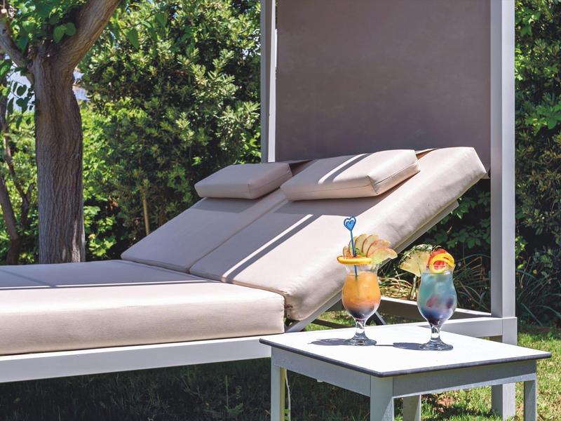 Dos tumbonas cómodas con cojines junto a una mesa pequeña con dos bebidas decoradas al aire libre.