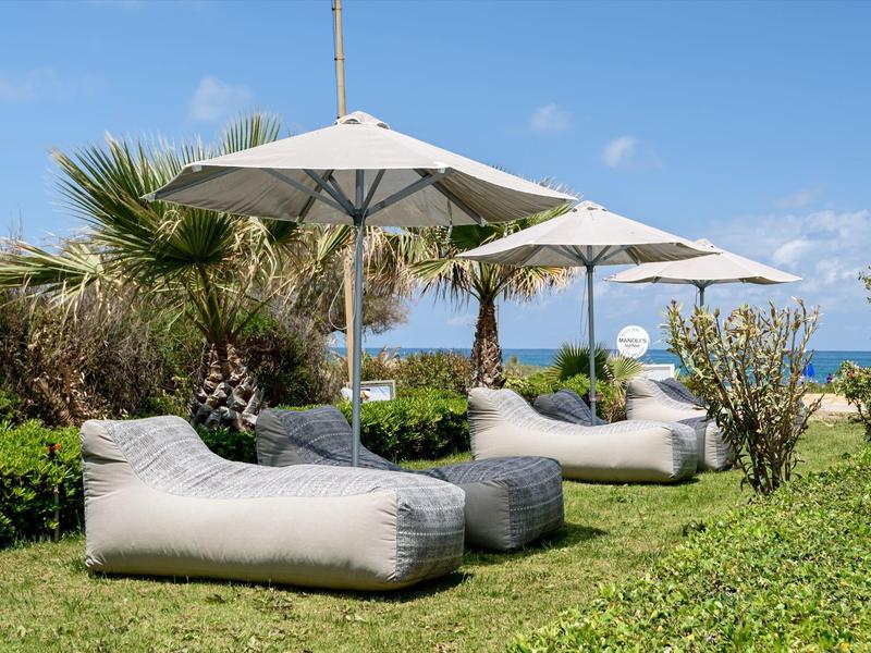 Sillones cómodos con sombrillas en césped con palmeras bajo cielo azul.