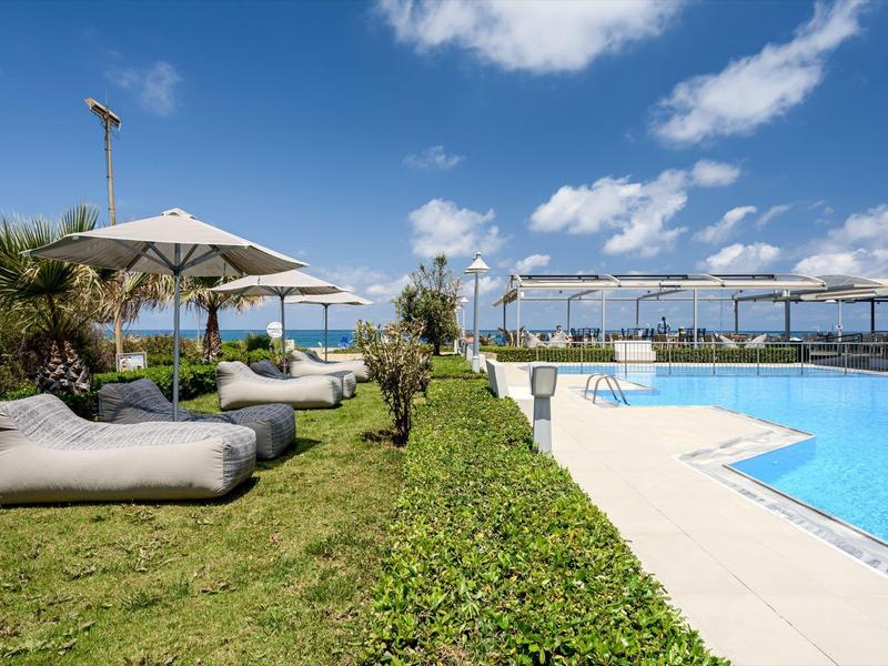 Piscina del hotel con tumbonas en césped bajo un cielo azul y soleado.