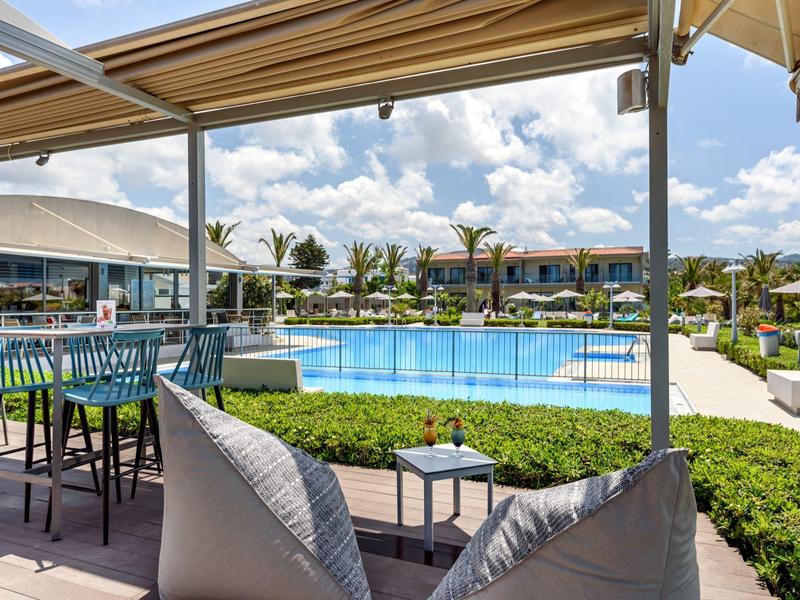 Área exterior moderna con piscina, asientos y bar en un hotel de lujo con clima soleado.