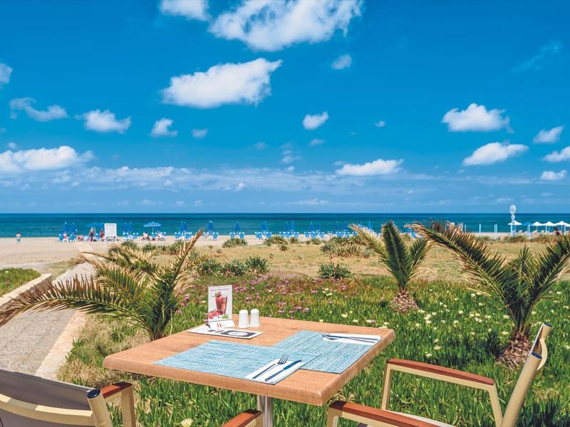 Una mesa puesta con vista al mar, rodeada de palmeras y césped verde en una playa soleada.