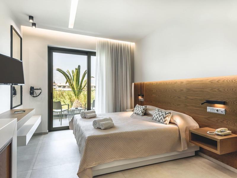 Habitación de hotel luminosa con cama doble, balcón y equipamiento moderno.